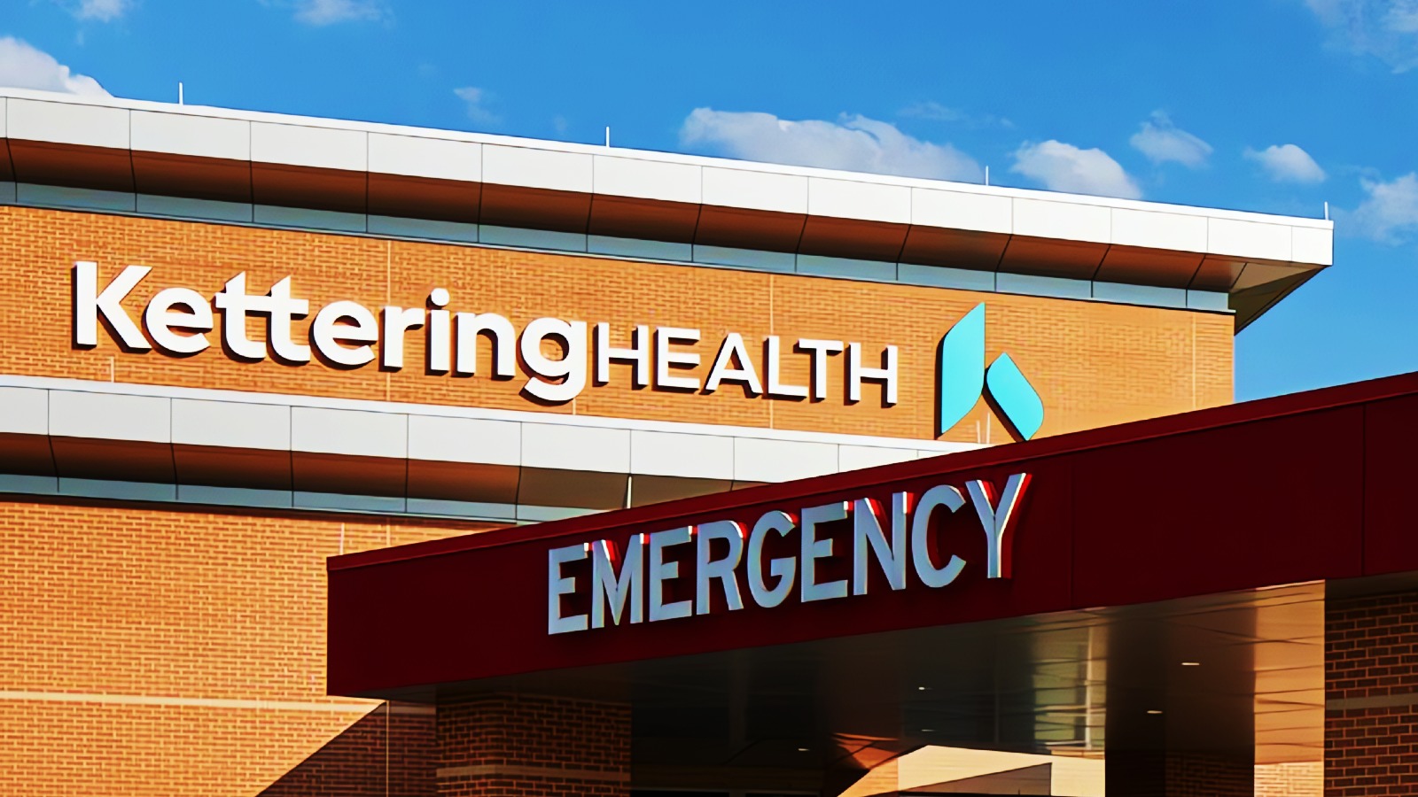 A building with a sign reading "Kettering Health" and an emergency entrance under a blue sky.